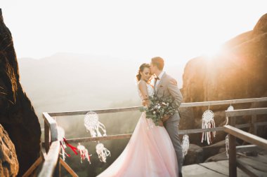 Yeni evli çift, gelin ve damat öpüşüyor, mükemmel dağ manzarasında sarılıyorlar, mavi gökyüzü.