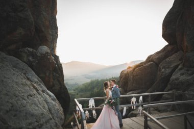 Yeni evli çift, gelin ve damat öpüşüyor, mükemmel dağ manzarasında sarılıyorlar, mavi gökyüzü.