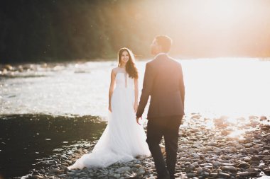 Zarif, şık, mutlu, sarışın gelin ve dağlardaki güzel bir nehrin arka planında harika bir damat..