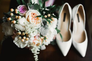 Gelinlerin düğün ayakkabıları, bir buket gül ve diğer çiçeklerle.