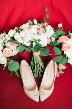 Bir çift zarif ve şık gelinlik ayakkabısı, alyansları, bir buket gülleri ve diğer çiçekleri var..