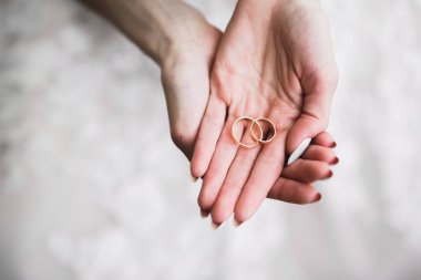 Zarif beyaz elbiseli güzel bir gelin elinde alyanslar tutuyor.,