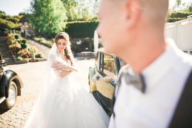 Gelin ve damat, zarif bir çift retro düğün arabasının yanında kalıyor..