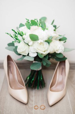 Bir çift zarif ve şık gelinlik ayakkabısı, alyansları, bir buket gülleri ve diğer çiçekleri var..