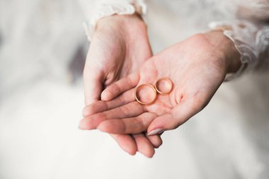 Zarif beyaz elbiseli güzel bir gelin elinde alyanslar tutuyor.,