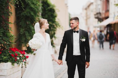 Düğün fotoğrafı çekimi. Gelin ve damat şehirde yürüyorlar. Birbirlerine sarılıp bakan evli bir çift. Tutma buketi.