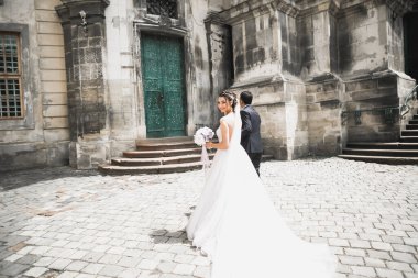 Düğün fotoğrafı çekimi. Gelin ve damat şehirde yürüyorlar. Birbirlerine sarılıp bakan evli bir çift. Tutma buketi.