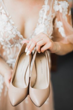 Zarif beyaz elbiseli güzel gelin ellerinde düğün ayakkabıları tutuyor..