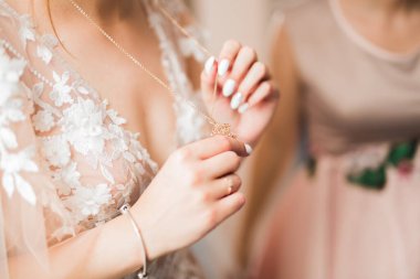 Zarif beyaz elbiseli güzel gelin elinde altın bir kolye tutuyor..