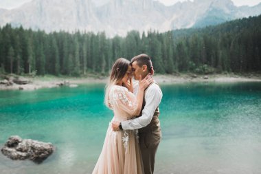 Doğadaki düğün çifti, dağlardaki güzel bir gölün yanında birbirlerine sarılıyorlar beyaz elbiseli güzel model kız. Takım elbiseli adam.