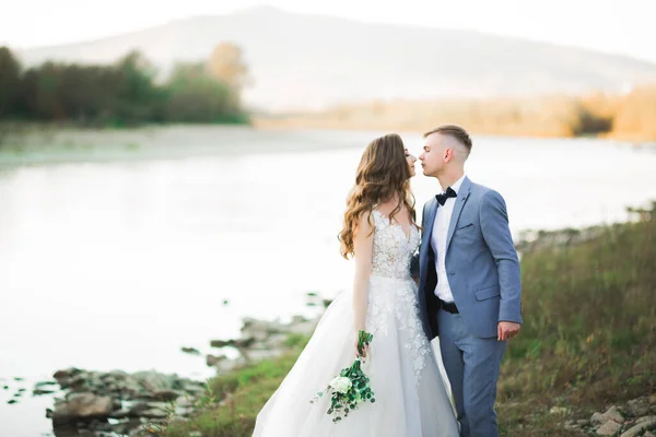 山の美しい川の背景にエレガントなスタイリッシュな幸せなブロンドの花嫁と豪華な新郎 — ストック写真