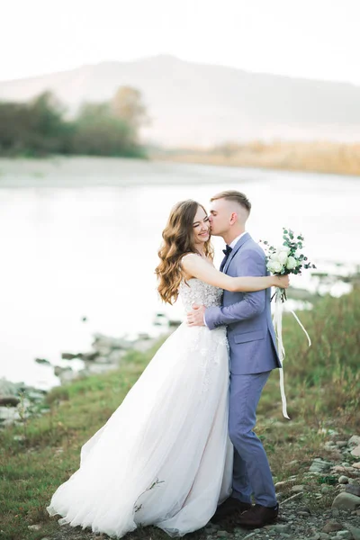 美丽的新婚夫妇亲吻着 拥抱着山河畔的石头 — 图库照片