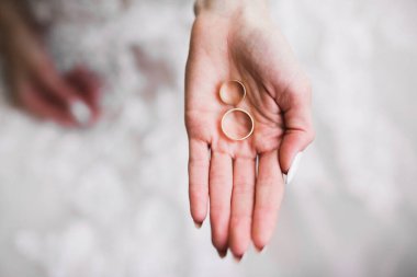 Zarif beyaz elbiseli güzel bir gelin elinde alyanslar tutuyor.,