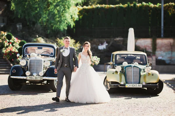 新婚夫妇 漂亮的新娘和优雅的新郎手牵着手 在复古的婚礼车附近互相望着对方 — 图库照片