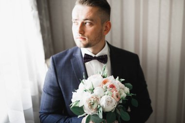 Güzel adam, damat elinde çiçeklerle büyük ve güzel bir düğün buketi tutuyor.