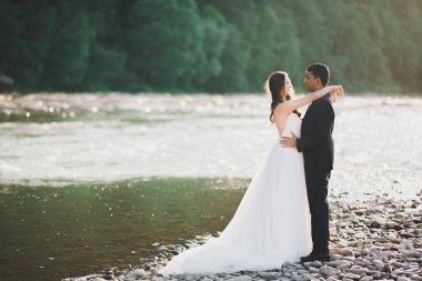 Doğadaki düğün çifti birbirine sarılıyor. Beyaz elbiseli güzel bir kız. Takım elbiseli adam.