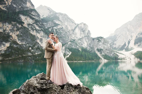 自然の結婚式のカップルは山の中で美しい湖の近くにお互いに抱き合っている 白いドレスの美しいモデルの女の子 スーツの男 — ストック写真