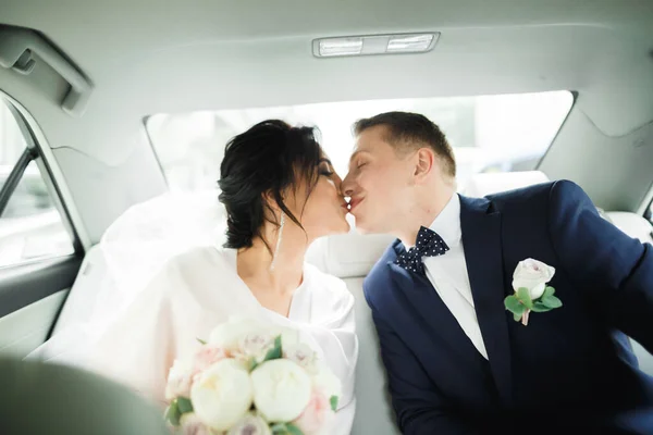 美しい花嫁と新郎の抱擁とキスで彼らの結婚式の日に車 — ストック写真