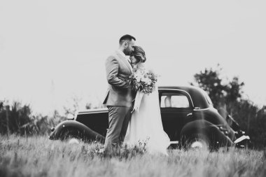 Şık bir düğün çifti, gelin, damat retro arabada öpüşüyor ve sarılıyor..