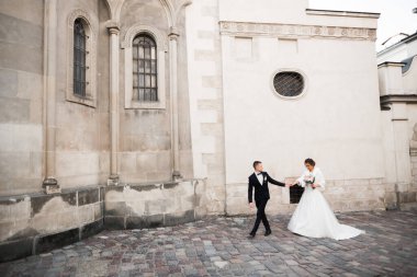 Düğün fotoğrafı çekimi. Gelin ve damat şehirde yürüyorlar. Birbirlerine sarılıp bakan evli bir çift. Tutma buketi.