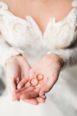 Zarif beyaz elbiseli güzel bir gelin elinde alyanslar tutuyor.,