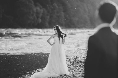 Zarif, şık, mutlu, sarışın gelin ve dağlardaki güzel bir nehrin arka planında harika bir damat..