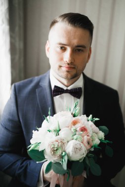 Güzel adam, damat elinde çiçeklerle büyük ve güzel bir düğün buketi tutuyor.