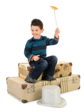 Kotlu ve çizgili kazaklı izole bir çocuk eski bavulların üzerinde oturmuş değnekle oynuyor..