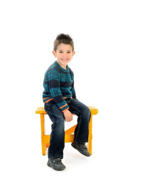 Sarı koltukta oturan yalnız çocuk gülümsüyor.