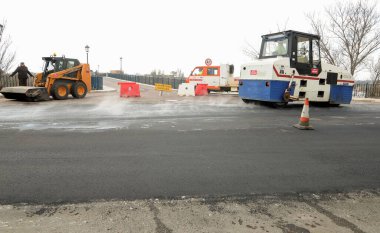 Machines performing asphalting and paving work on a city road.