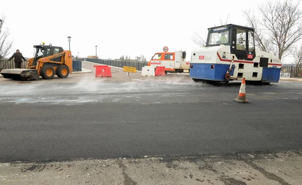 Machines performing asphalting and paving work on a city road.