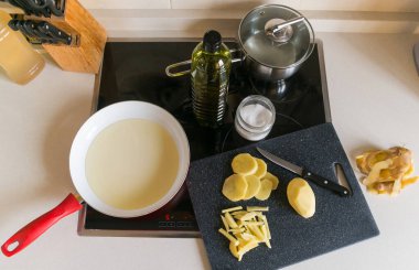 Çiğ soyulmuş ve patatesleri tavada kızartılmak üzere hazırlanmış ve yukarıdan seramik bir hob üzerinde sıcak yağla izlenmiş..