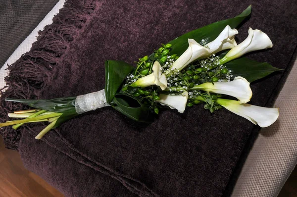 Bouquet of calla lilies or gannets. Zantedeschia aethiopica. White flowers. Close up view of the bouquet on a brown blanket.