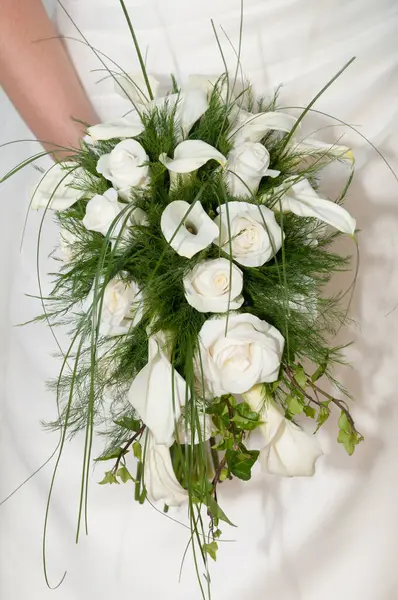 Bouquet of calla flowers and white roses. Zantedeschia aethiopica. Lilies. Coves. Roses. The arm of a woman dressed in white clothes grasps the bouquet on her wedding day.