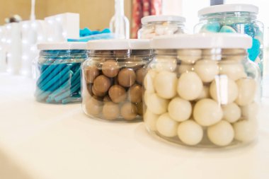 Cam kavanozlar içinde şeker ve çikolata, mavi, kahverengi ve beyaz renkler, bir partide masanın üzerinde. Mavi şekerlerle kahverengi şekerlerin arasına odaklan..