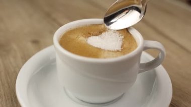 Metal kaşık, siyah espresso americano kahveli beyaz bardağa şeker koyar.