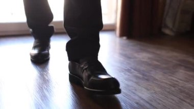 Bir adam siyah ayakkabılarla odada yürür.