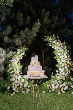 Romantik ışıklarla aydınlatılmış şık katlı bir düğün pastası, çiçeklerle süslenmiş bir arka planda.