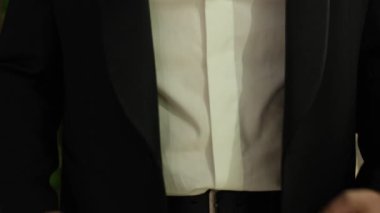 Siyah takım elbiseli bir adam ceketinin düğmesini bağlar.