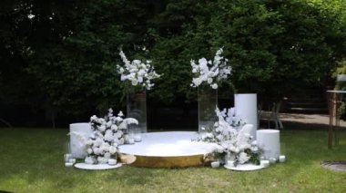 Serin bir bahçede sergilenen çarpıcı bir çiçek kemeri ve beyaz sandalyeli açık hava düğün töreni.