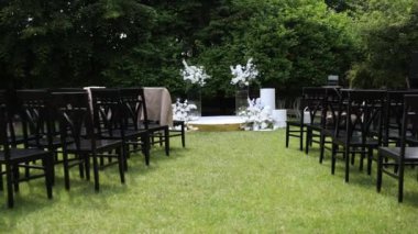 Serin bir bahçede sergilenen çarpıcı bir çiçek kemeri ve beyaz sandalyeli açık hava düğün töreni.