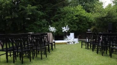 Serin bir bahçede sergilenen çarpıcı bir çiçek kemeri ve beyaz sandalyeli açık hava düğün töreni.