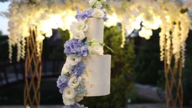 Düğün kemerinin yanında büyük beyaz bir düğün pastası.