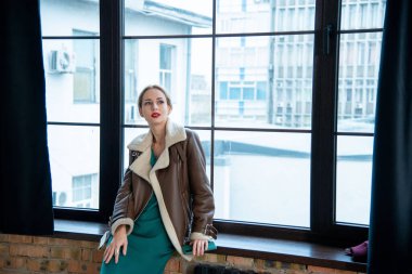 Güzel sarışın kadın pencerenin yanında poz veriyor.