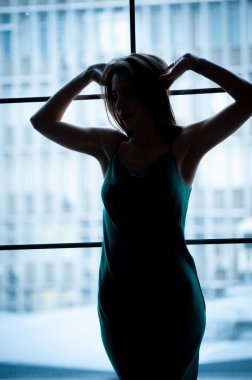 Yeşil elbiseli genç ve güzel bir kadın, panoramik pencerenin yanında poz veriyor.