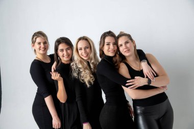 Sisters posing in studio, wearing black dresses against white background. Girls smiling and having fun.