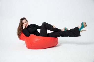 beautiful young woman in black clothes posing on bean bag chair on a white background