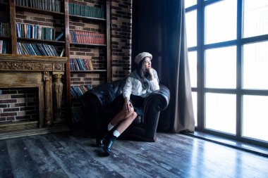 portrait of a woman wearing beret sitting on a chair with books