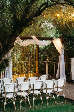 Çiçek süslemeleri ve yumuşak ışıklandırmayla süslenmiş zarif masaların bulunduğu güzel dekore edilmiş bir düğün yeri, özel kutlama için romantik ve büyüleyici bir atmosfer yaratıyor..