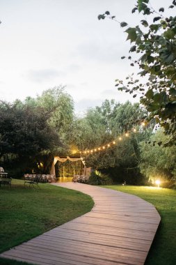 Çiçek süslemeleri ve yumuşak ışıklandırmayla süslenmiş zarif masaların bulunduğu güzel dekore edilmiş bir düğün yeri, özel kutlama için romantik ve büyüleyici bir atmosfer yaratıyor..